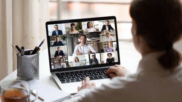 The back of a woman while she looks at a laptop with twelve people on a zoom call