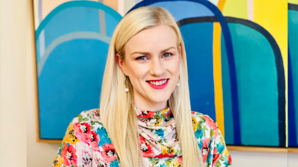 Richelle McCausland sits with her arms folded in front of a bright image