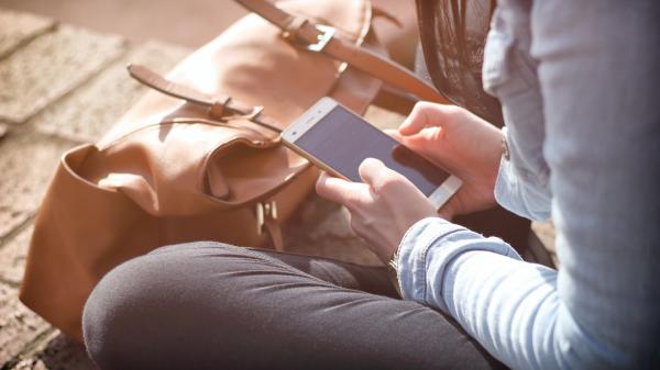 Young person sits cross-legged on her phone with her bag in front of her