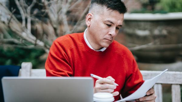 Man in red jumper reads with a laptop in front of him