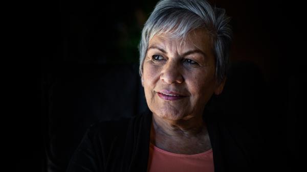 A woman with grey hair smiles knowingly out from a black background