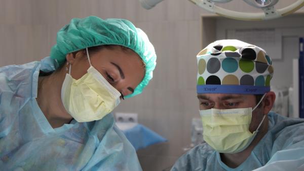 A man and woman in personal protective equipment look intently at what they are doing