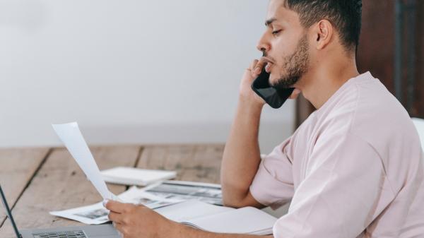 Young man concentrates while speaking on the phone and looking at a document in his hand