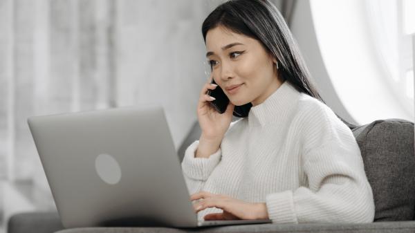 Woman on the phone in a white shirt smiles at her laptop