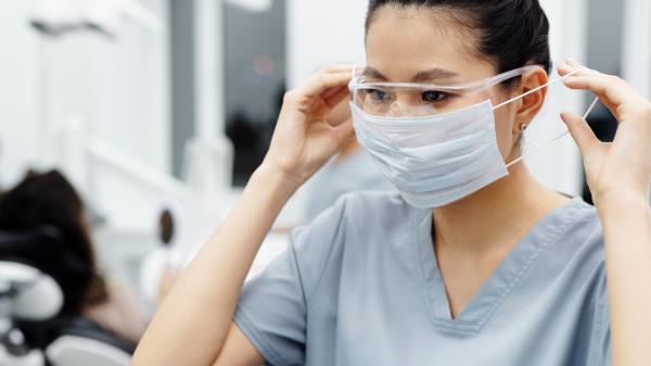 A woman tucks her mask strings behind her ears in scrubs
