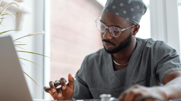 Man in personal protective equipment types while carefully considering a laptop screen
