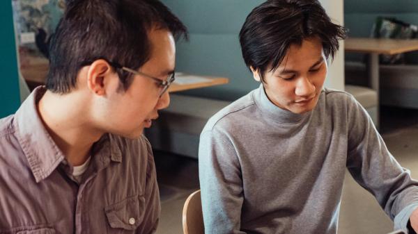 Two young men in a classroom setting look at something in front of them