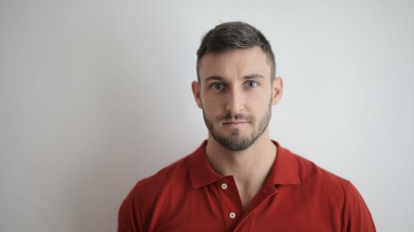 A man's bright red shirt stands out against a white background as he stares into the camera