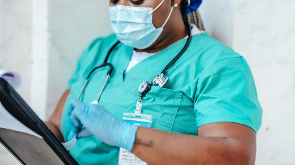 A woman in scrubs and a mask looks at something in her hands as she touches it with her gloved hand