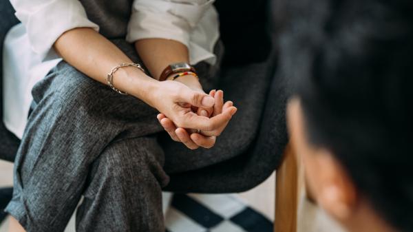 Hands are clasped on the knees of a woman in smart casual attire