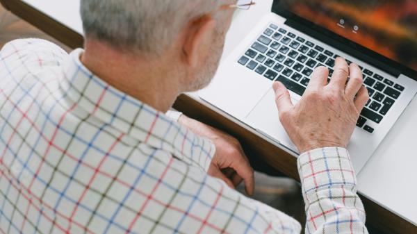 We see over the shoulder of a man onto his hand on his computer keyboard