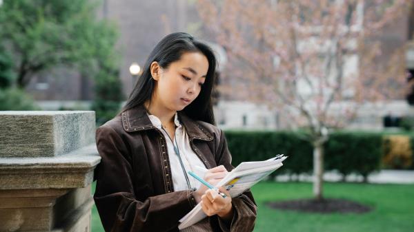 Young woman stands in a park reading from a notebook