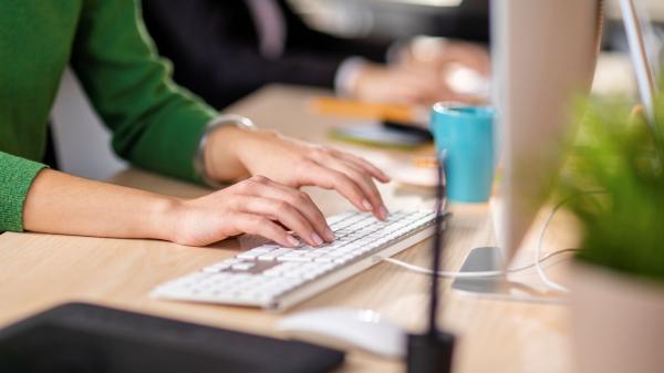 A woman in a green shirt types on a computer keyboard