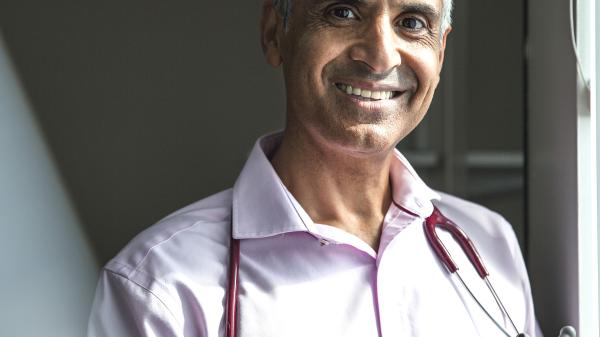 A man smiles at the camera with a stethoscope around his neck