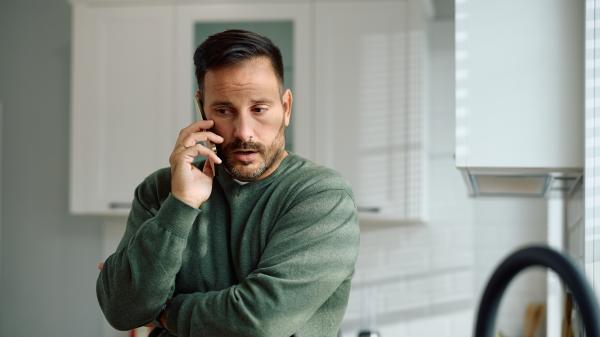 A man speaks on his phone, one arm crosses his body