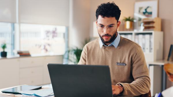 Against an office background, a man types on his laptop
