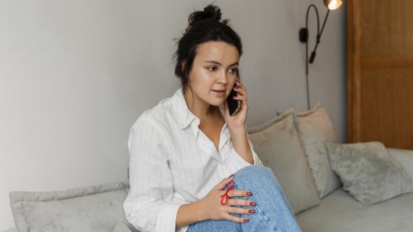A young woman talks on the phone while sitting on a couch, her hand on her leg