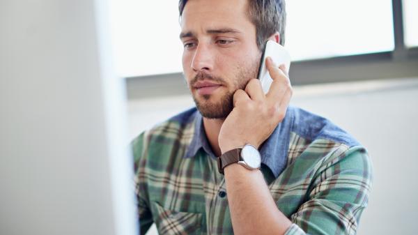 On the phone, a man looks worriedly at a computer screen