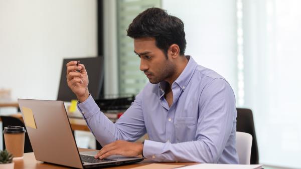Sitting at a desk, a man thinks while looking at his laptop