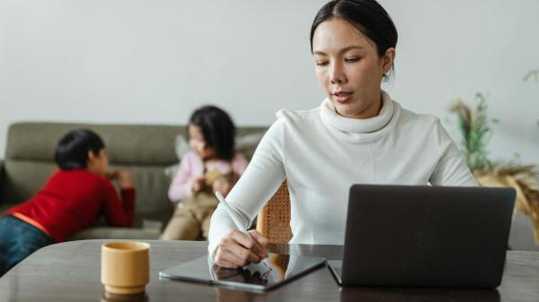 A woman sits at desk with her laptop, working through an issue on a notepad