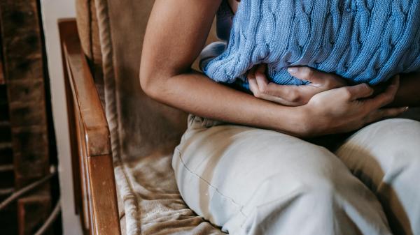 A woman sits in a chair, holding her stomach tightly