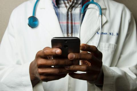 Person in white lab coat with stethoscope uses their mobile phone