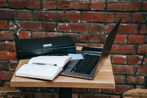 Black laptop sits open with a notebook and folder on a small table