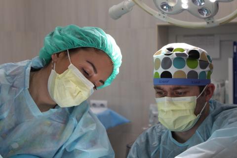 A man and woman in personal protective equipment look intently at what they are doing