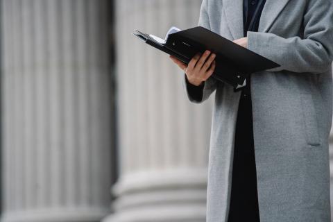 Professional woman in a grey coat reads a report in front of white pillars
