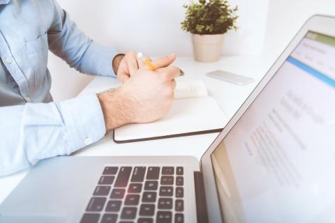 Clasped hands rest behind an open laptop