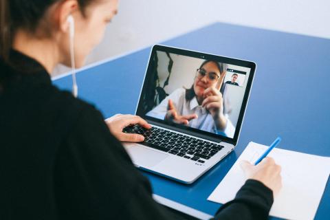 Woman in black looks at a laptop screen where a young woman is speaking