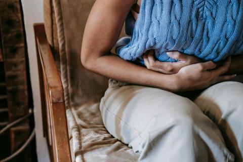 A woman sits in a chair, holding her stomach tightly
