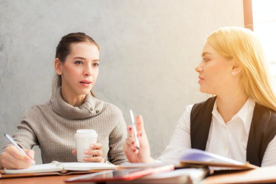 Two women speak under the glow of sunshine from outside