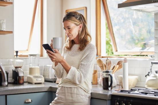 A woman surveys her phone leaning against a corner in a breezy kitchen