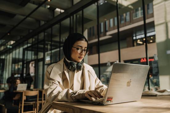 Woman with a hijab and headphones examines her computer screen